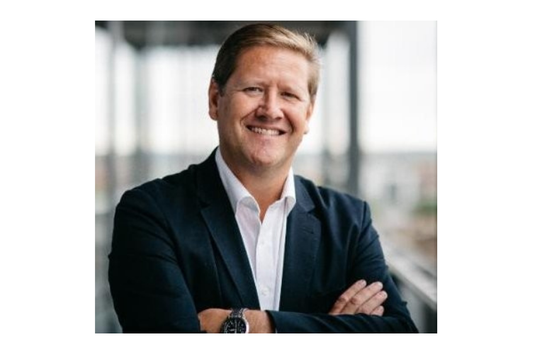 Image of Andy dressed in a black suit he is folding his arms smiling at the camera