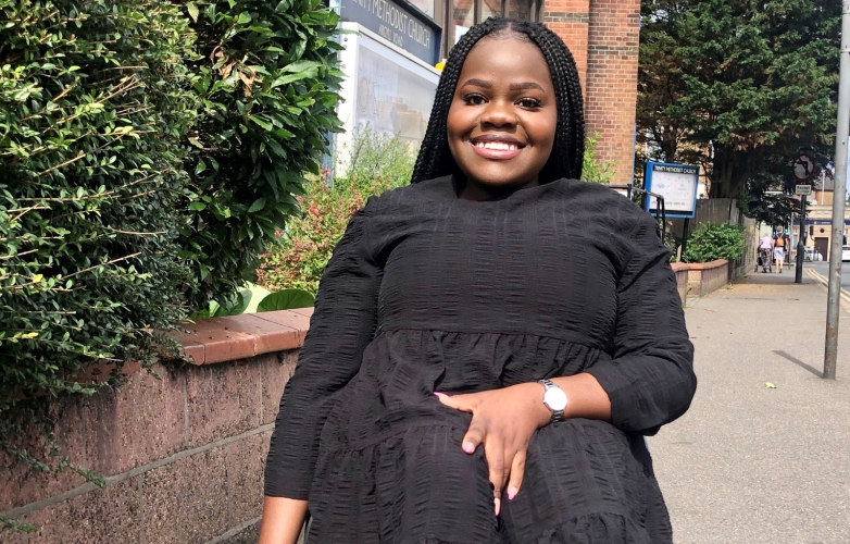 Image shows Nom dressed in a smart black dress sitting in her wheelchair outside smiling at camera