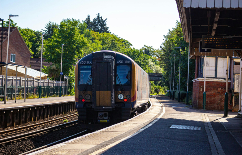A train platform outside in sunshine and shade with a train in the distance coming towards the camera to stop at the platform