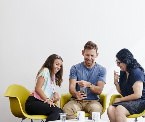 Three people sitting on yellow chairs looking at a phone